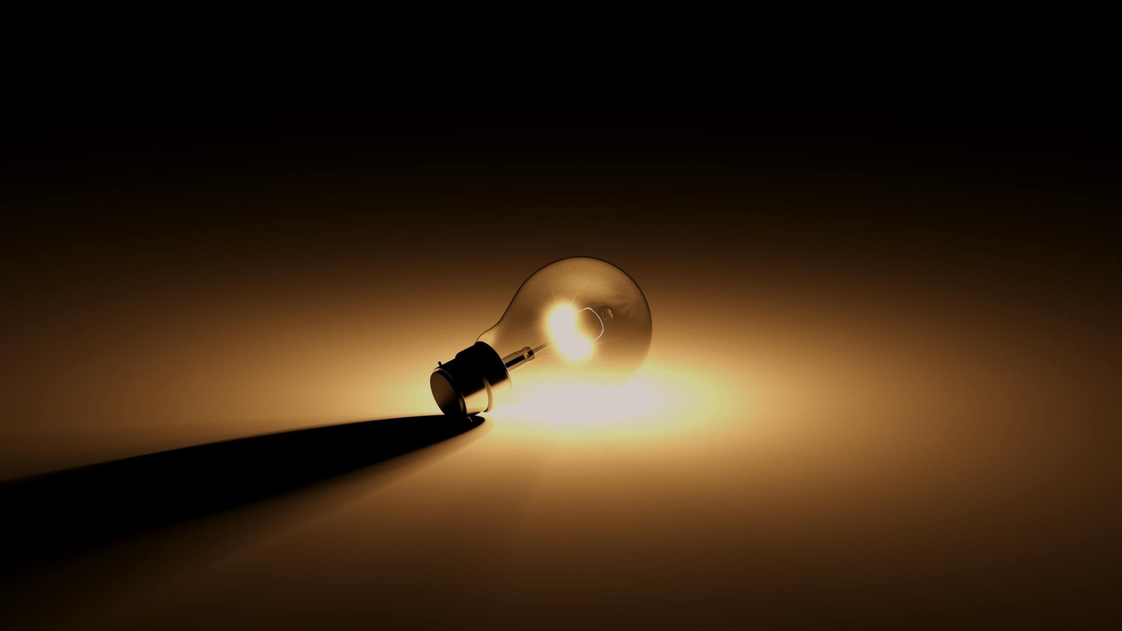 A close-up of an illuminated light bulb lying on a surface, casting a warm glow.